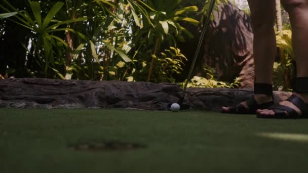 En ung kvinna som spelar minigolf. Benen i ramen. Mitten skott. Skjut bollen i hålet — Stockvideo