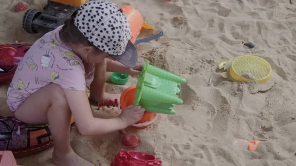 Petite fille jouant dans un bac à sable avec sable et jouets — Video