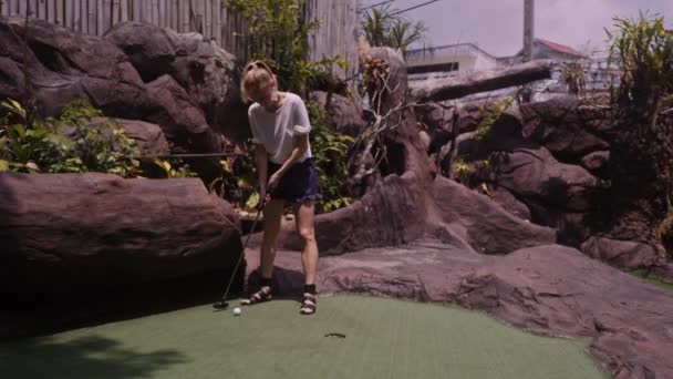 Een jonge vrouw die Minigolf speelt — Stockvideo