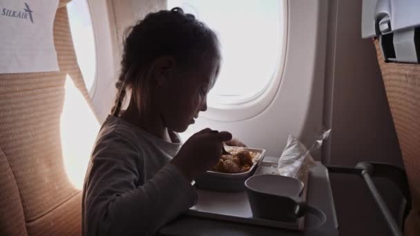 Barnet flyger på ett flygplan för att vila. En tjej som sitter nära fönstret och äter — Stockvideo