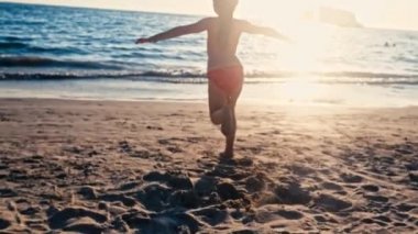 Güzel gün batımı ışık denize çalışan mutlu çocuk silüeti. Kumlu plaj, dikiz, ağır çekim suya doğru acele bebeğim