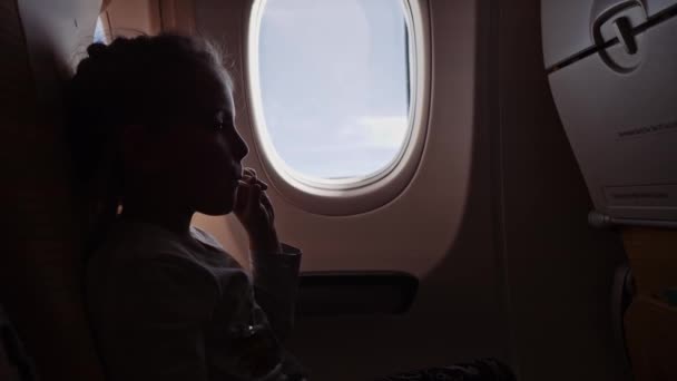 Χαριτωμένο κορίτσι με γλειφιτζούρι κάθεται στο αεροπλάνο. — Αρχείο Βίντεο
