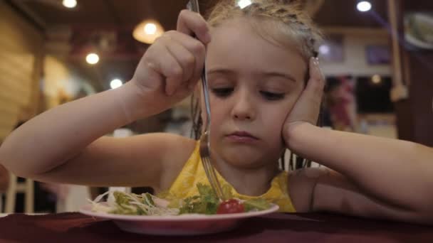 Маленька дівчинка їсть зелений салат з апетитом у ресторані. Концепція хорошого здоров'я — стокове відео