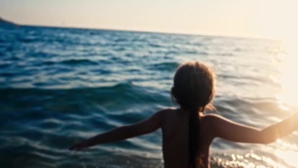 Silhouette eines glücklichen Kindes, das bei schönem Sonnenuntergang ins Meer läuft. Baby stürmt am Sandstrand auf Wasser zu, Rückansicht, Zeitlupe — Stockvideo