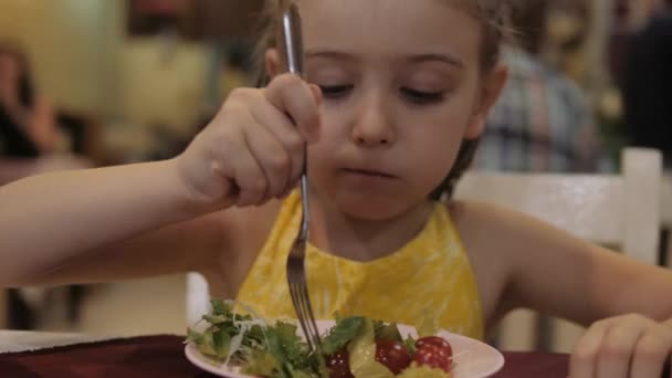 小さな女の子はレストランで食欲を持ってグリーンサラダを食べます。良い健康の概念 — ストック動画