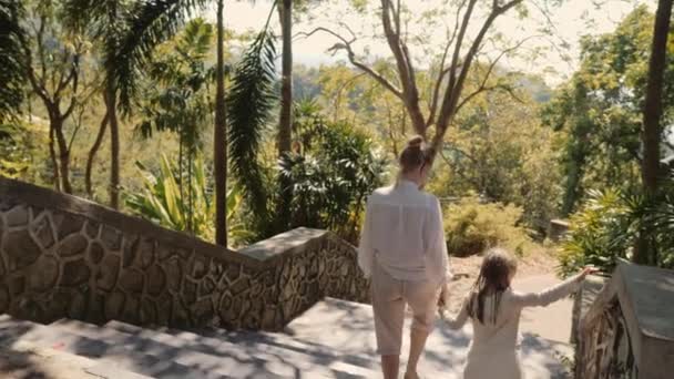 Tiempo en familia. Madre e hija bajan a pie por el camino del campo en la colina de la isla tropical. Punto de vista escénico — Vídeo de stock