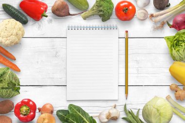 Boş defter ve kalem sebze beyaz mutfak masasında ile çevrili.