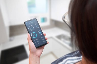 Kadın kullanım akıllı ev kontrol app modern cep telefonunda. Arka planda ev iç.
