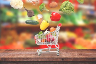 Vegetables fall in market cart on wooden table.  Market with fresh vegetables in background. clipart