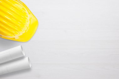 Kask ve planları inşaat alanı üzerinde beyaz ahşap masa üzerinde. Metin için sağ tarafta boş alan.