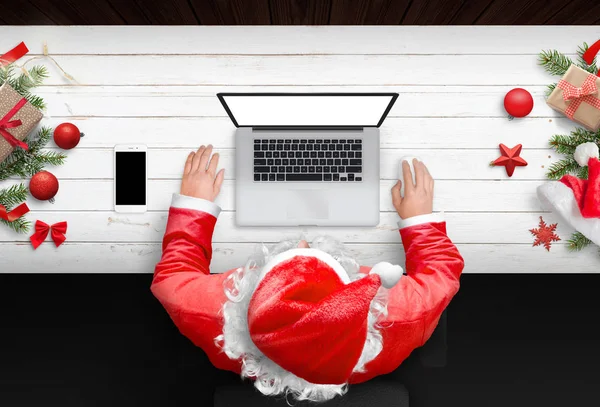 サンタ クロースは モックアップの孤立した画面のラップトップ コンピューターで動作します クリスマスの時期 クリスマスの装飾と木の机 携帯電話の横にあります トップ ビュー — ストック写真