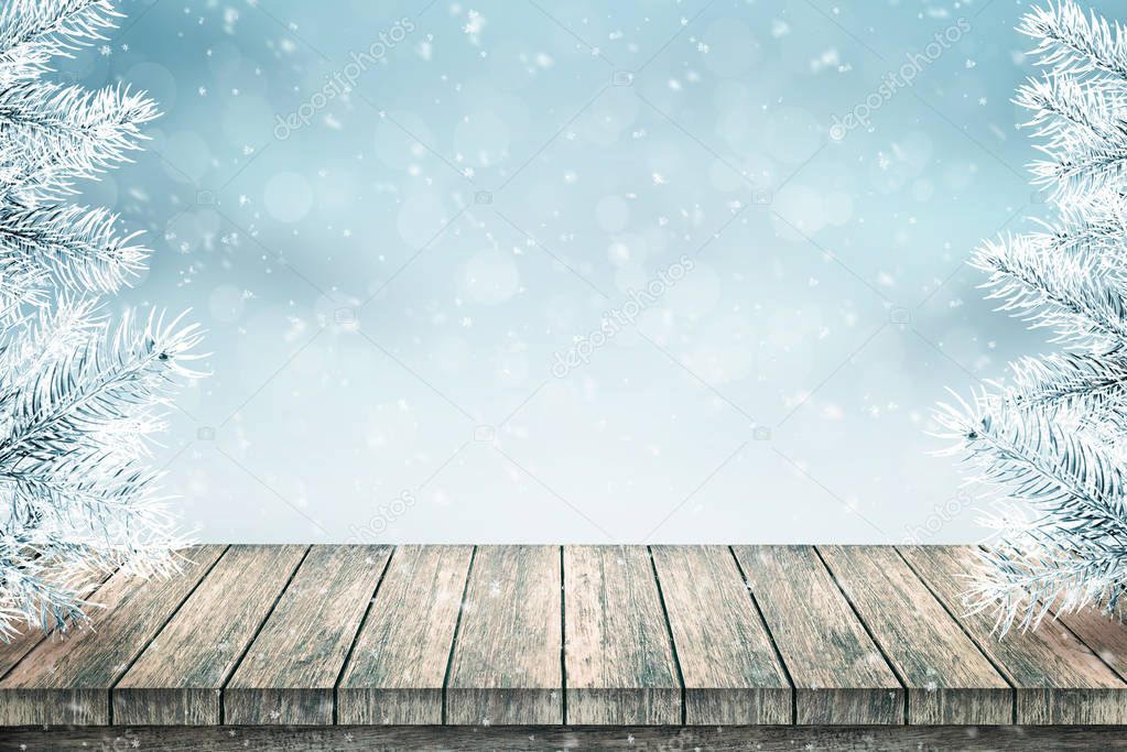 Empty wooden table and Christmas fir trees covered with snow. Snow falls. Blue background.