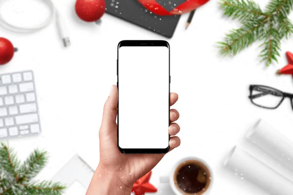 現代の携帯電話のモックアップです 手持ち株のスマート フォン オフィスの机の上のバック グラウンドでのクリスマスの装飾 — ストック写真