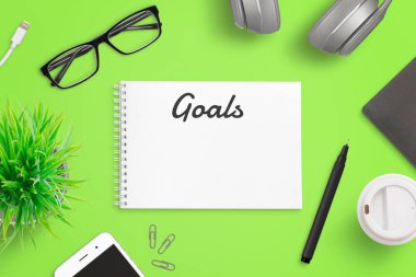 Not defteri sayfası konseptine hedefler yazmak. Akıllı telefonu, gözlüğü, dosyası, kahvesi, bitkisi olan yeşil ofis masası. Üst görünüm bileşimi.