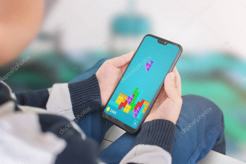 Boy play popular tetris game on his mobile phone. Close-up view over the shoulder.