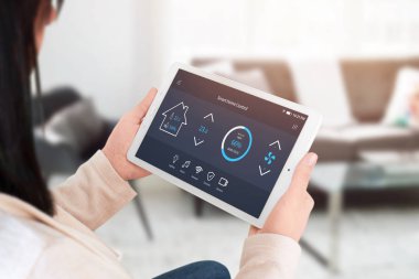Akıllı ev kontrol app kadın elinde tablet ekranda. Ev, oturma odası iç arka planda.