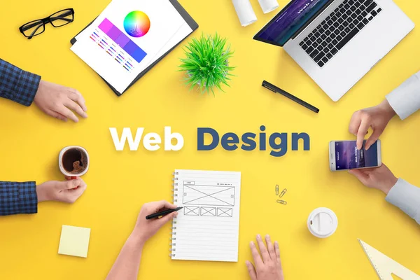 Web design team work on project concept. Yellow desk with web design text. Top view, flat lay.