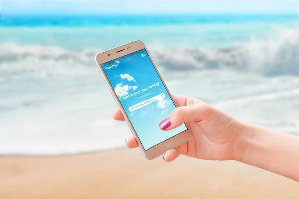 Woman use travel app on smart phone to find next travel destination. Beach and sea in background. Close-up.