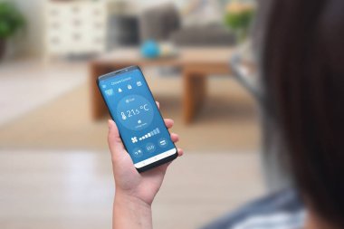 Kadın sıcaklık ve havalandırma ayarlamak için oturma odasında bir telefonda iklim kontrol uygulaması kullanın.