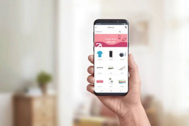 Modern bir akıllı telefonda çevrimiçi mağaza uygulamasını el ile gösteriyor. Online alışveriş ve kapmak fırsatlar, indirimli pazarlama kavramı. Ürün kategorileri ve alışveriş sepeti.