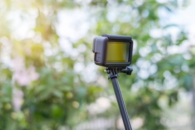 Tripod üzerinde aksiyon kamerası, selfie çubuğu görüntüleri yapar. Sahteiçin boş creen. Arka planda ağaç.