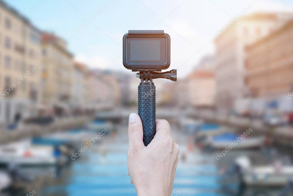 Action camera on stick in hand recording city concept. Blank screen for mockup.