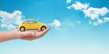 Elinde sarı araba ile araba sigortası kavramı. Arka plandaki bulutlar. Alanı yanındaki kopyala.