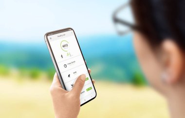 Kız adım uzunluğu ve yakılan kalori ölçmek için cep telefonu uygulaması kullanır. Modern düz tasarım telefon uygulaması konsepti. Arka planda doğa manzarası.