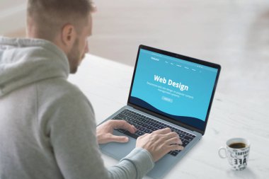 Web tasarımcısı bir tanıtım sitesi konsepti üzerinde çalışıyor. Ofis masası, yakın çekim. Düz dizayn web sitesi dizüstü bilgisayar ekranında.