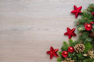 Ahşap yüzeyde süslemeleri olan bir Noel arkaplanı. Boşluğu, düzlüğü, üst görünüm bileşimini kopyala. Köknar ağacında kırmızı parlak toplar, yıldızlar ve çam kozalakları.