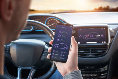 Motoru, lastikleri ve pil durumu bilgisi olan akıllı araba uygulaması. Sürücünün cep telefonu var. Arka planda direksiyon ve tahta görüntüsü