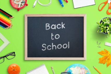 Tebeşirle yazılmış yazı tahtası okul malzemeleriyle çevrili. Yeşil çalışma masasındaki üst görünüm kompozisyonu