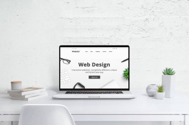 Web tasarımı stüdyo yaratıcı konsepti. Şirket web sitesi olan modern dizüstü bilgisayar, düz dizayn temalı konsept. Bitkiler ve kitaplarla dolu beyaz ahşap masa.