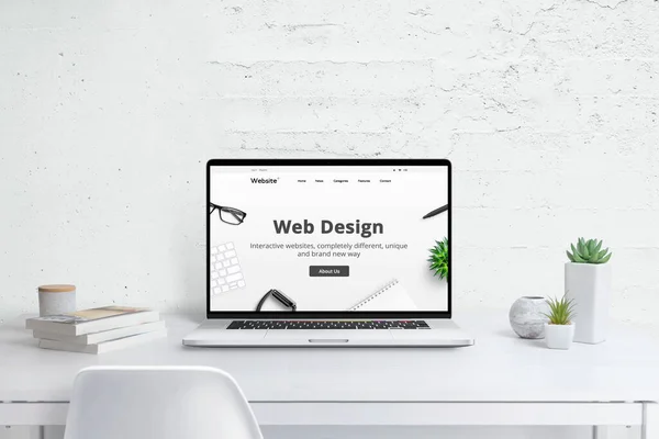 Web design studio creative concept. Modern laptop computer with company web site, flat design theme concept. White wooden desk with plants and books