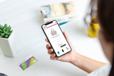 Akıllı telefon konseptiyle internetten alışveriş yapan kız. Modern apartman tasarımı ürünleri web sitesi. Kredi kartı arka plandaki masada.