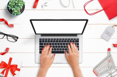 Etrafı alışveriş eşyalarıyla çevrili bir dizüstü bilgisayar. Üst manzara, alışveriş çantası, el arabası, satış rozeti ve hediye kutusu olan düz masa.