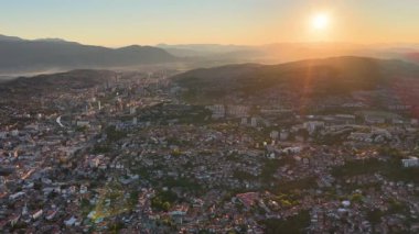 Saraybosna 'nın günbatımında şehir ve dağların üzerinden yükselen parlayan güneşli görüntüleri