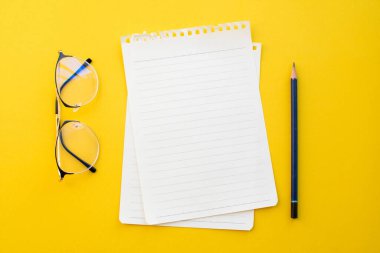 Okul konseptiyle sarı zemin üzerinde gözlük ve kalem boş kağıt.
