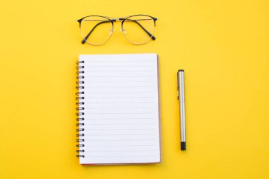 Okul konseptiyle sarı zemin üzerinde gözlük ve kalem boş kağıt.