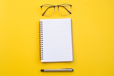 Okul konseptiyle sarı zemin üzerinde gözlük ve kalem boş kağıt.