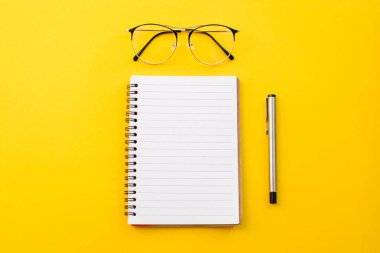 Okul konseptiyle sarı zemin üzerinde gözlük ve kalem boş kağıt.