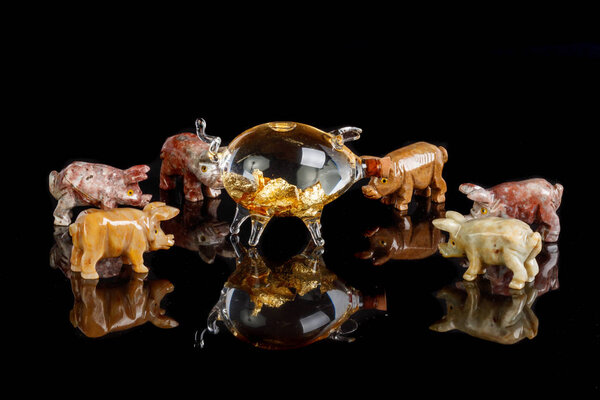 Свиные фигурки из оникса, яшмы, стекла, золота на черном фоне крупным планом
