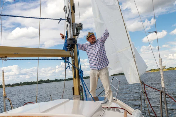 sailor man in a cap on a boat under sail against the sky and wat