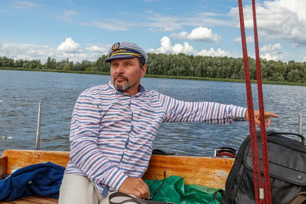 sailor man in a cap on a boat under sail against the sky and wat