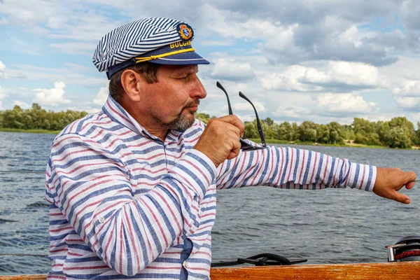 sailor man in a cap on a boat under sail against the sky and wat