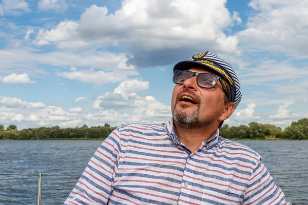 sailor man in a cap on a boat under sail against the sky and wat