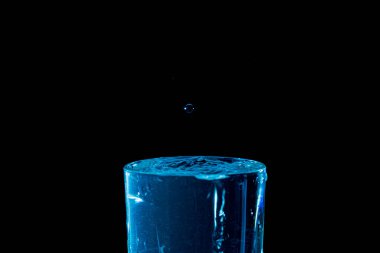 Su damlası düşüyor, makro sıçrama. Doğal ve karanlık bir arkaplanda yakın plan.