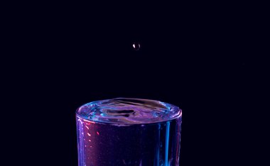 Su damlası düşüyor, makro sıçrama. Doğal ve karanlık bir arkaplanda yakın plan.