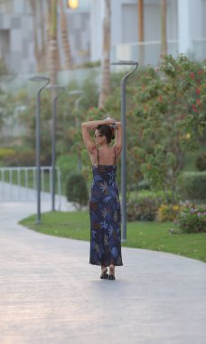 Uzun, ince esmer kadın portresi. Tatil köyünde, koyu renkli, uzun elbiseli.