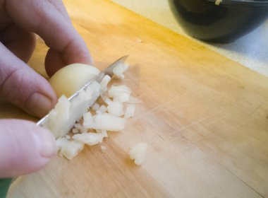 Soğan yemek pişirmek için hazırlanan ve küçük küpler halinde bir ahşap tahta üzerinde keskin bir bıçak ile kesmek.